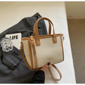 Detail of woven beige bucket bag with brown leather trim and adjustable shoulder strap