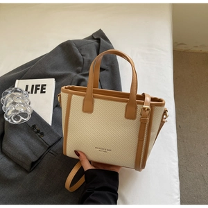Detail of woven beige tote bag with brown leather handles and adjustable buckle strap