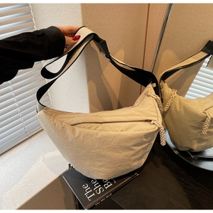 Detail of beige nylon crescent bag with adjustable black strap and textured zipper pull