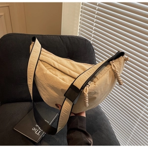 Detail of cream nylon crescent bag showing soft pleated texture and woven shoulder strap