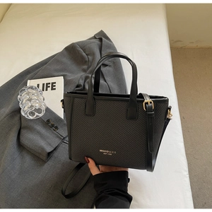 Detail of black woven bucket bag with gold lettering shown next to a blazer and book
