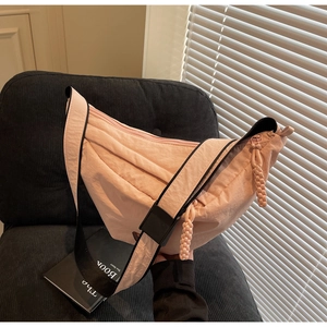 Detailed view of pink nylon crescent bag with woven zipper pull on a dark fabric surface