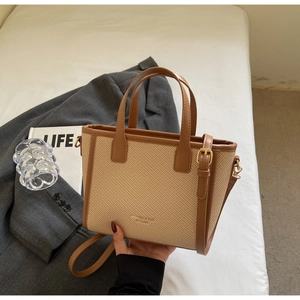 Detail of woven beige tote bag with brown leather handles and golden metal hardware