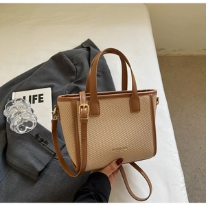 Detail of woven straw tote bag with brown leather handles and adjustable shoulder strap