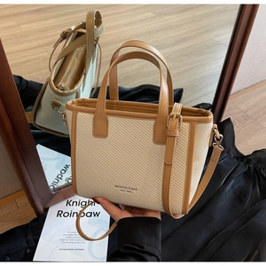 Close-up of woven tote bag with brown leather trim and gold hardware details