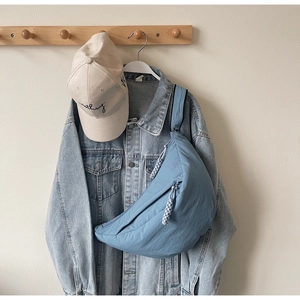Close-up of a light blue crescent crossbody bag styled with a denim jacket and cap