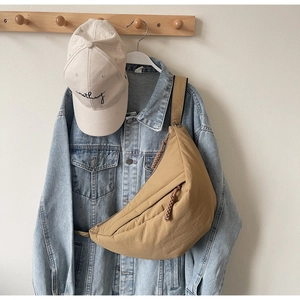 Detail of khaki crescent crossbody bag with woven zipper pull on casual outfit background