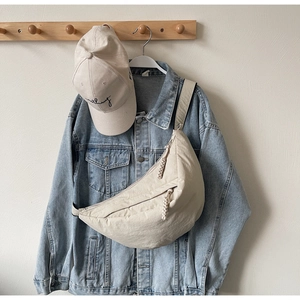 Close-up of beige crescent bag with woven zipper on denim jacket outfit