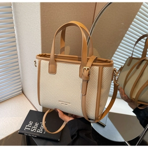 Chic cream woven bucket bag with brown leather handles held by a model in a warm room