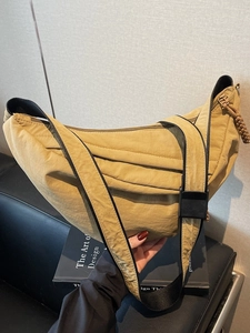Khaki crescent nylon crossbody bag with adjustable strap on a modern leather background
