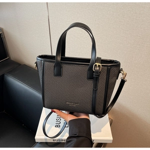 Detail of grey woven tote bag with black leather handles and gold logo on books