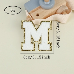 Macro detail of Chenille letter M patch with gold sequins and white embroidery texture