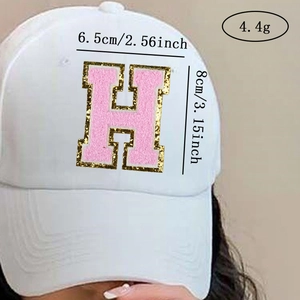 Close-up of pink chenille letter H patch with gold glitter edge on a white baseball cap