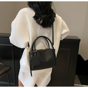 Detail of black lychee grain leather bucket bag with puppy charm and shoulder strap
