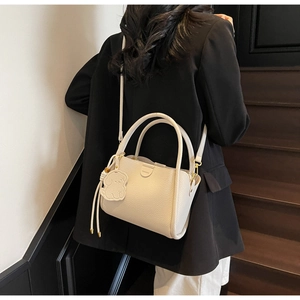Rear view of cream leather bucket bag with dog charm on model in black blazer