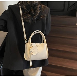 Chic cream bucket bag with dog charm shown in a lifestyle indoor setting over the shoulder