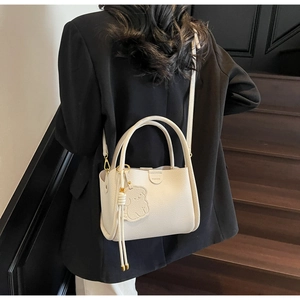 Close-up of cream lychee leather tote featuring a fashion plate and cute bear charm