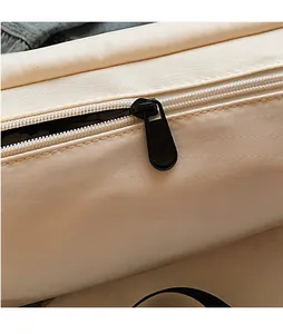 Detail of a sleek black teardrop-shaped metal zipper head on a beige canvas messenger bag