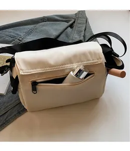 Close-up of cream nylon messenger bag showing functional front zipper pocket storage