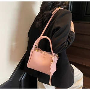 Pink lychee texture leather bucket bag with dog charm on model in studio setting