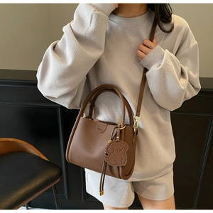 Brown bucket bag with pebble texture, fashion logo, and a cute dog charm in lifestyle setting