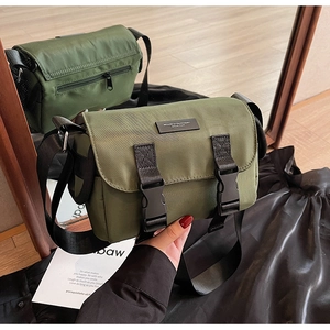 Detail of dark green nylon messenger bag featuring black buckle straps and brand tag