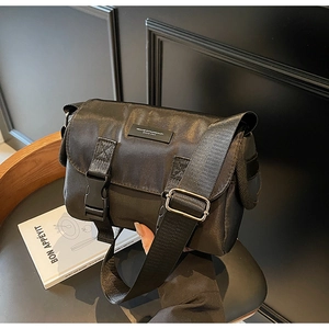 Detail of black nylon messenger bag with flap cover, dual buckles and rubber logo patch