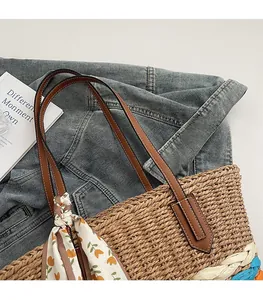 Dettaglio borsa tote in paglia con manici in pelle marrone e sciarpa floreale arancione