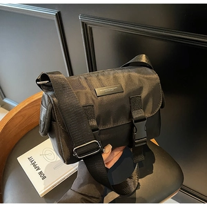 Detail of black nylon messenger bag featuring double buckles and wide woven shoulder strap