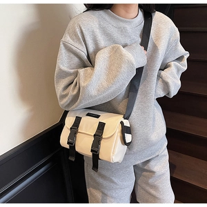 Detail of off-white messenger bag with black buckles on adjustable nylon strap