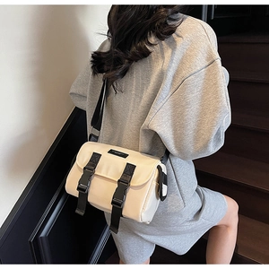 Model wearing a minimalist cream messenger bag with black buckles on outdoor stairs