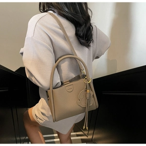 Detail of khaki lychee leather bucket bag featuring a cute dog charm on indoor stairs