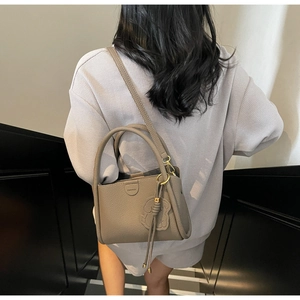Detail view of taupe litchi texture leather bucket bag with cute dog charm and fashion tag