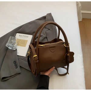 Close-up of brown pebbled leather bucket bag with fashion label and bear charm accessory