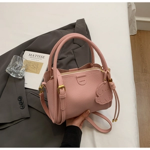 Pink lychee grain leather bucket bag with puppy charm on a grey blazer backdrop