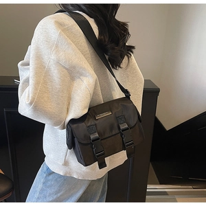 Detail view of a black nylon messenger bag with buckle straps worn by a model