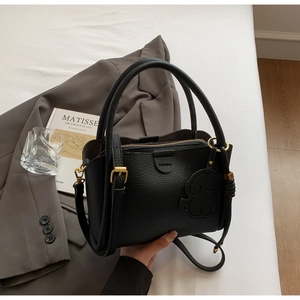 Detail of black lychee grain leather bucket bag with gold hardware and dog charm decoration