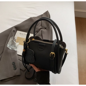 Detail of black lychee grain handbag with gold hardware and chic puppy bag charm