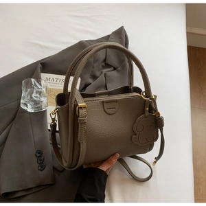Detail of lychee pattern leather handbag with puppy charm and fashion brand logo