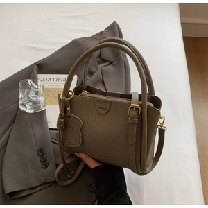 Detail of tan litchi grain leather bucket bag featuring a cute puppy charm and gold hardware