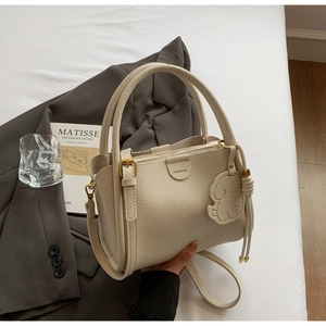 Detail of beige lychee leather bucket bag with puppy charm on grey suit background