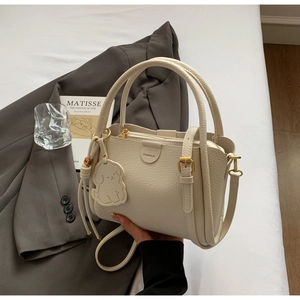 Detail of beige lychee grain leather bucket bag with cute dog charm and fashion logo
