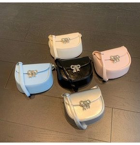 Flat lay of five fashionable saddle bags in multiple colors with silver bow buckles