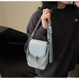 Detail of light blue crossbody bag with woven texture, metal turn-lock and adjustable strap