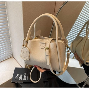 Detail of cream lychee leather bucket bag featuring fashion embossing and a cute puppy charm
