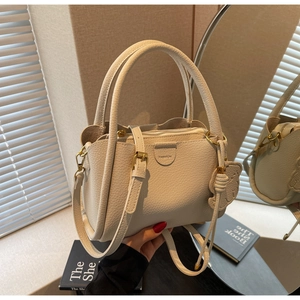 Close-up of beige lychee grain leather bucket bag with dual handles and bear charm