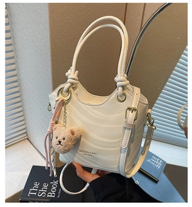 Detailed view of white wavy texture bucket bag with gold hardware and plush bear charm