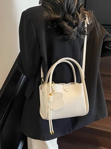 Elegant white lychee leather bucket bag with top handles and bear charm on shoulder