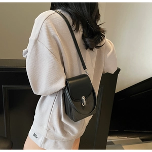 Detailed side view of a black crossbody bag with silver buckle worn by a model