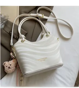 Detail of cream white shoulder bag with wave texture, gold ring handle and bear charm
